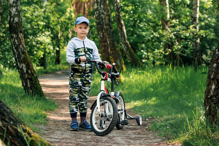在上自行车在清晨森林的孩子。男孩在头盔户外骑自行车