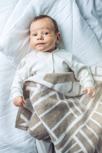 可爱有趣的婴儿躺在一张覆盖着毯子的白床上。母性的柔情与家庭价值的概念