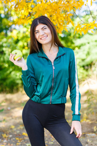 一个年轻的女孩，在一套运动服户外拥有一个绿色的苹果。美丽的体育女人吃水果