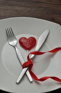 一把刀绑在一块红色的丝带上, 白色的盘子上显示一个红色的心形棒糖