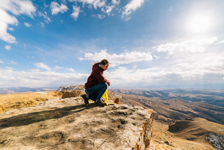 活跃的年轻女孩沿高加索山脊旅行, 坐在山的边缘