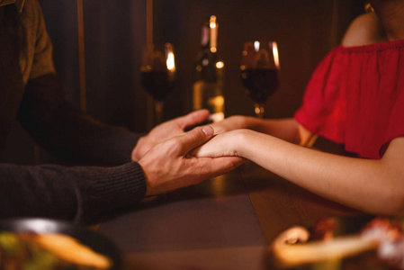 年轻的情侣在餐厅, 浪漫的约会。优雅的女人在红色的礼服和英俊的男人吃饭和手牵着手, 特写