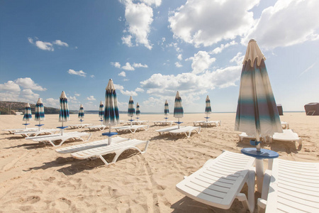许多沙滩椅和封闭遮阳伞上美丽的海滩与多云的蓝色天空