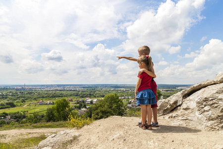 小儿童男孩和女孩站在山的岩石和展望未来。男孩表现出了他的手