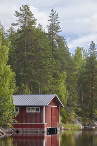 芬兰风景森林湖和红色木小屋。夏天