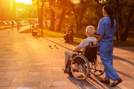 护士和老人坐在轮椅上看着美丽的夕阳在公园