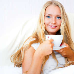 微笑的女人喝着咖啡躺在家里或酒店的床上。