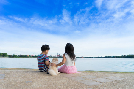 小男孩和逗人喜爱的女孩坐在水旁边与狗在蓝色 s