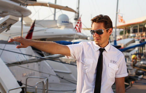 一个英俊的男人，一个穿着白色衬衫的严肃船长，在游艇附近