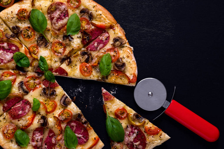 热和美味的比萨饼与意大利腊肠西红柿奶酪和蘑菇准备吃的黑色木制背景。顶部视图