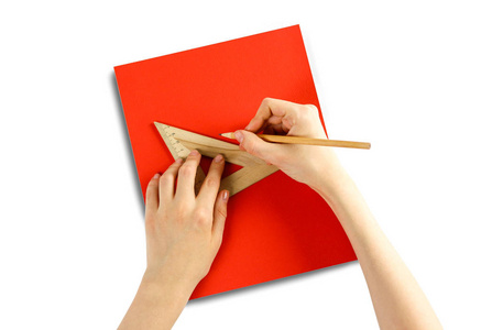 手拿着一个三角形的尺子和铅笔在一张红纸上。clos