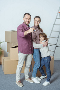 愉快的家庭与一个孩子微笑在照相机和拿着钥匙从新的公寓