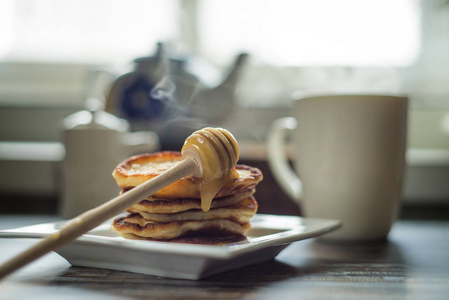 美味的早餐。自制的煎饼与蜂蜜和茶杯的木制质朴的背景表。复古风格怀旧色调的图像