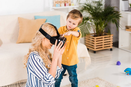 可爱的小男孩帮助母亲使用虚拟现实耳机在家
