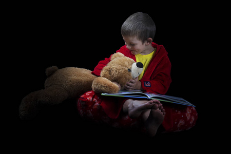 滑稽的男孩，在睡前时间读一本书的玩具熊
