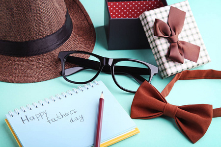 快乐父亲节写在笔记本上的领结, 眼镜, 帽子和礼品盒