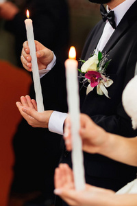 新郎在一个黑色的西装和新娘手持点燃的蜡烛