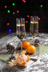 在一个白色的盘子上的新年餐桌上的橘子, 颠簸和眼镜, 香槟, 绿色的餐巾和新年的灯在黑暗的背景