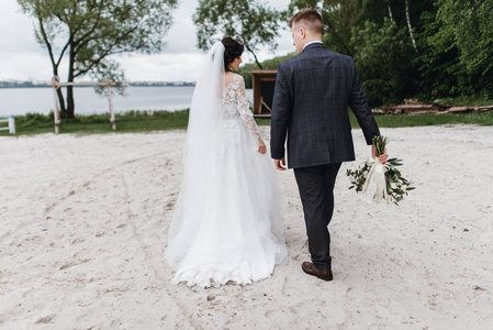快乐的年轻刚结婚的夫妇在他们的婚礼上漫步在河边海滩