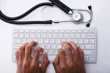 医生在电脑键盘上打字, 用听诊器在白桌上