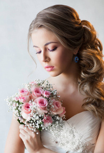年轻美丽的女人在白色的婚纱礼服摆在粉红色玫瑰花束的时尚肖像