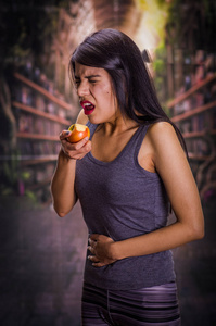 美丽而孤独的女孩患有小儿厌食症，痛苦在他的肚子时她正在吃一个苹果，在模糊的背景