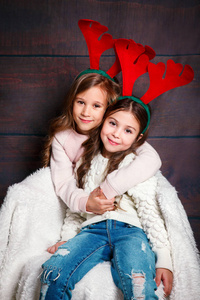 两个快乐的小女孩拥抱。圣诞节的概念。在演播室的鹿角微笑滑稽的姐妹