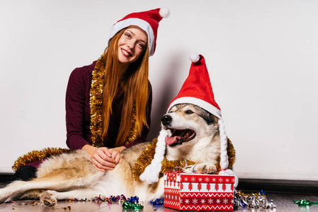 可爱的快乐 redhaired 女孩与红帽像圣诞老人坐在地板上, 她的狗庆祝新年2018