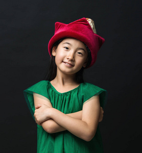 可爱的亚洲女孩在一个黑色的背景穿着童话帽子和绿色礼服