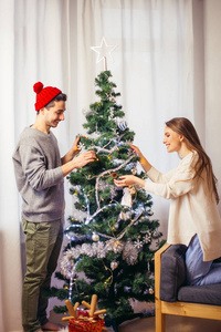 年轻幸福的情侣装饰圣诞树。自然光, 选择性聚焦