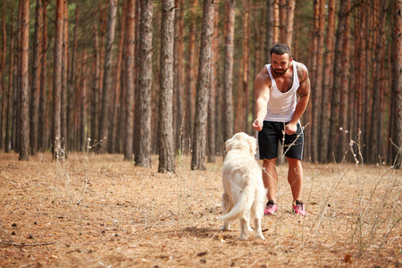 英俊的年轻男子与一只拉布拉多犬在户外在森林里