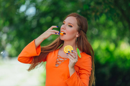 美丽的红色头发的妇女与多汁的美味橙在夏季绿色公园的肖像