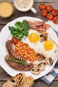 英式早餐。在木桌上煎蛋, 香肠, 培根, 豆子, 土司, 西红柿, 橙汁和咖啡杯。顶部视图