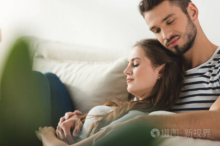 年轻的情侣睡在沙发上, 在家里拥抱