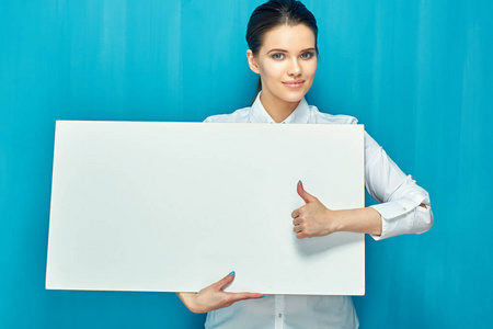 微笑的妇女拿着大白色标志板和显示拇指在蓝色墙壁背景