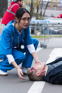 年轻的亚洲女医生帮助无意识受伤的男子躺在街上