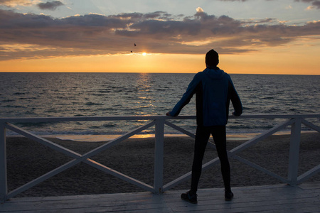 年轻男性赛跑者在海或海洋海滩在早晨, 反对日出