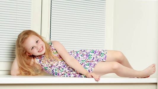 一个小女孩正坐在窗口与百叶窗帘