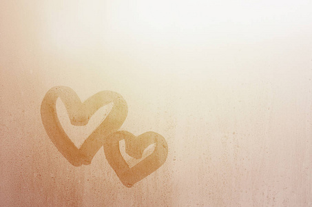 两个抽象模糊的爱心符号手画在湿窗玻璃与阳光背景。情人节明信片模板