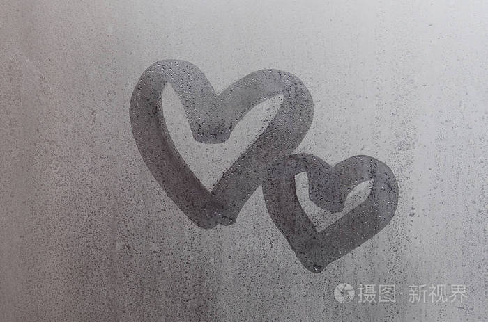 两个抽象模糊的爱心符号手画在湿窗玻璃与阳光背景.情人节明信片模板