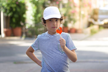 一个小男孩正站在街上用一只公鸡形的棒糖