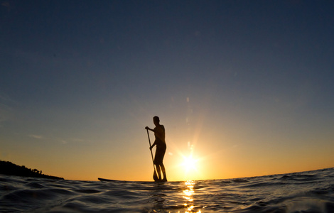 日落时分，一个人在冲浪板上划桨