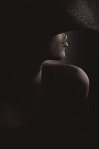 戏剧性的黑暗工作室的女人在黑色宽帽和黑色礼服的肖像。隐藏的半边脸