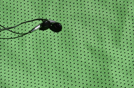 黑色耳机位于涤纶尼龙纤维的绿色运动装上。现代技术在运动训练中的听音乐概念