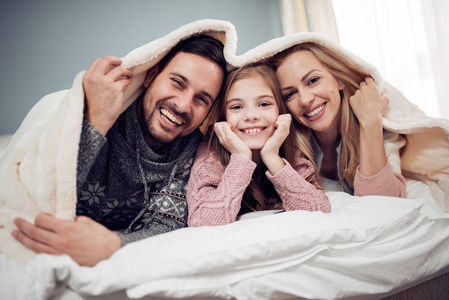 幸福的年轻家庭。母亲, 父亲和女儿在床上玩得很开心