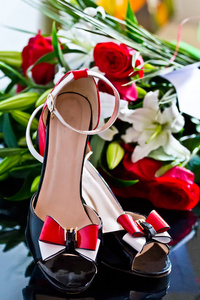 红色和白色蝴蝶结的美丽的鞋子在花安排附近红玫瑰和白色百合