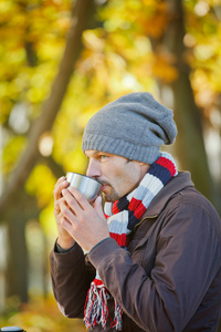 男人在秋天公园喝茶