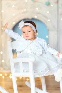快乐的小女孩穿着礼服, 坐在椅子上, 在节日的灯光背景