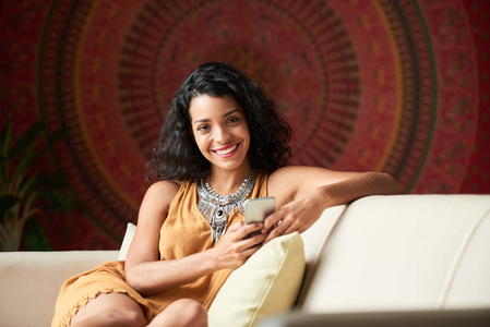 快乐的年轻拉丁妇女与智能手机在家休息