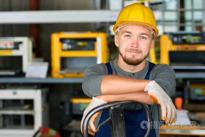 欢快的年轻工人的肖像穿着安全帽姿势看着相机和微笑享受工作在现代